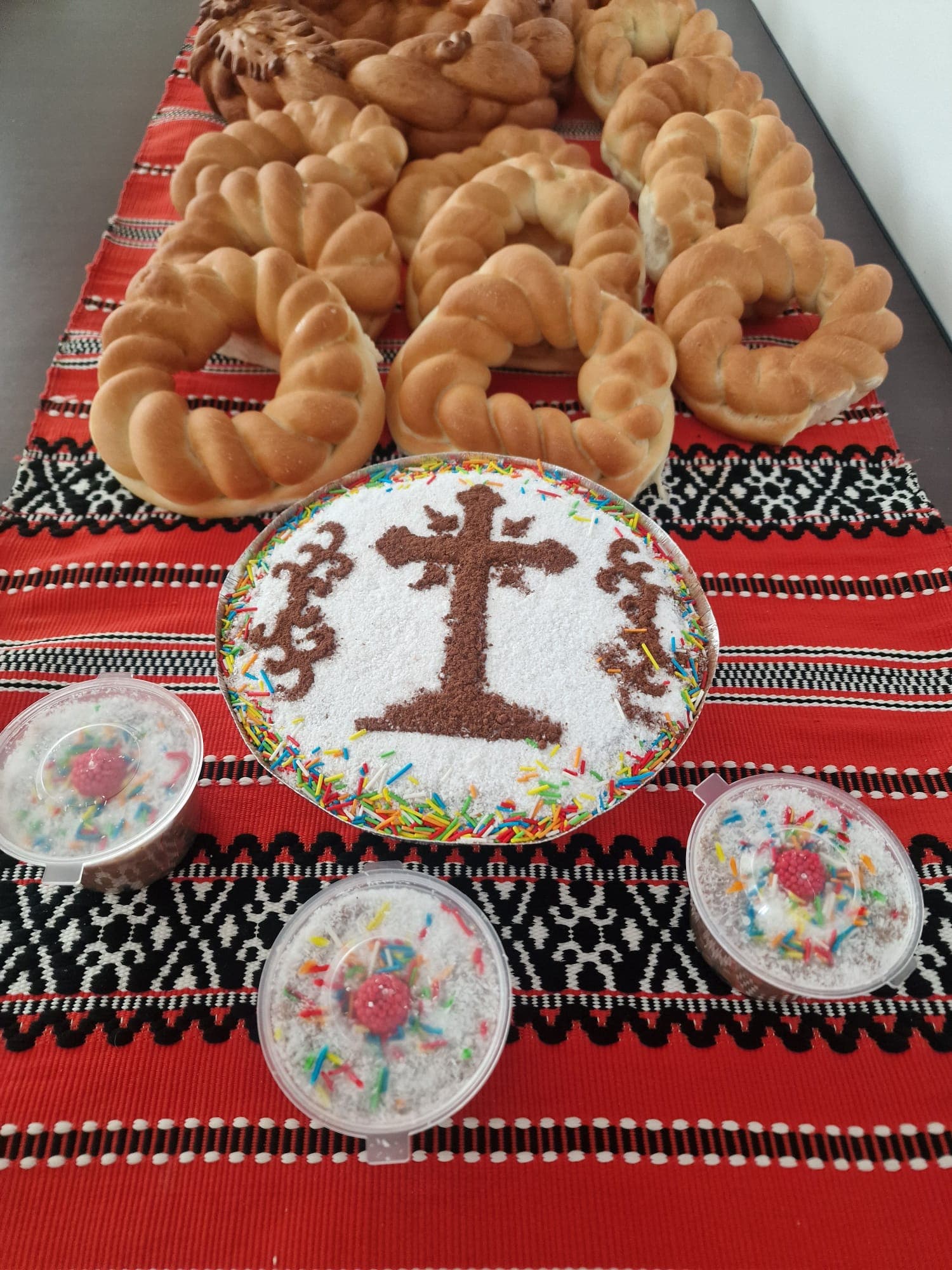 Colivă cu cruce din pesmet și zahăr pudră, alături de pahare individuale